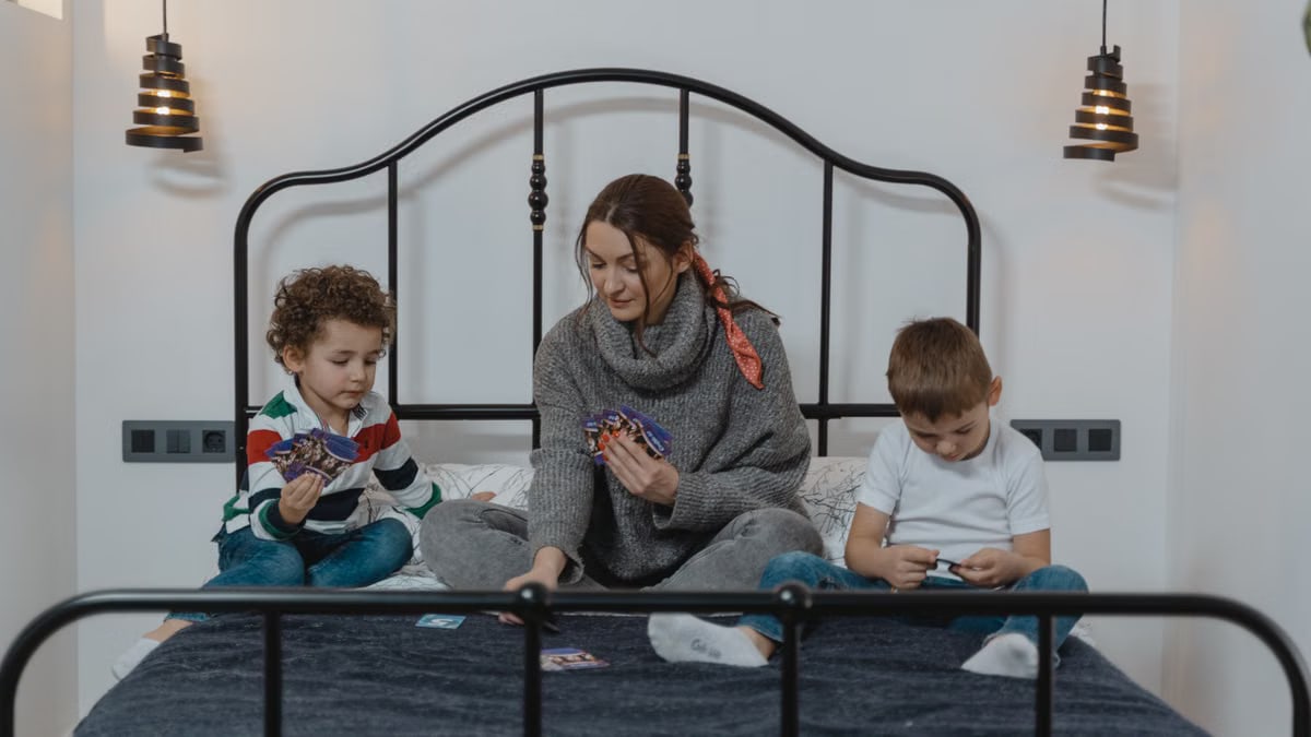 Mother and children play cards in cozy bedroom, enjoying quality bonding time.