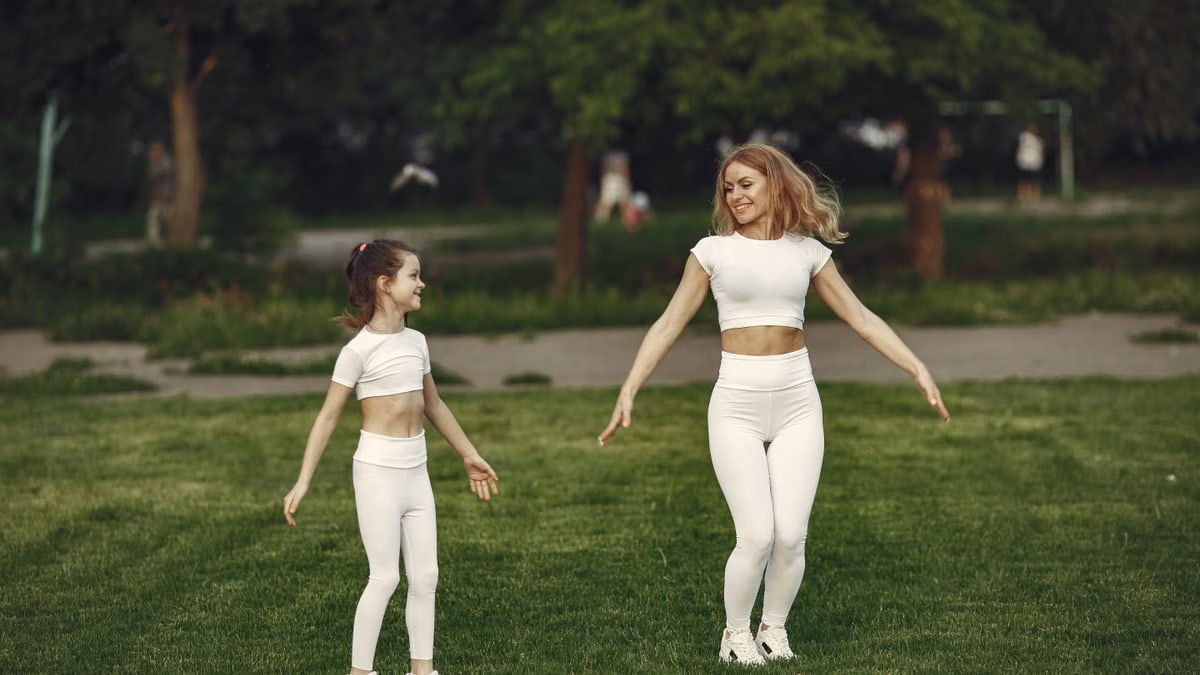 Mother and daughter bonding through outdoor exercise in activewear, featuring a joyful moment in a green park.